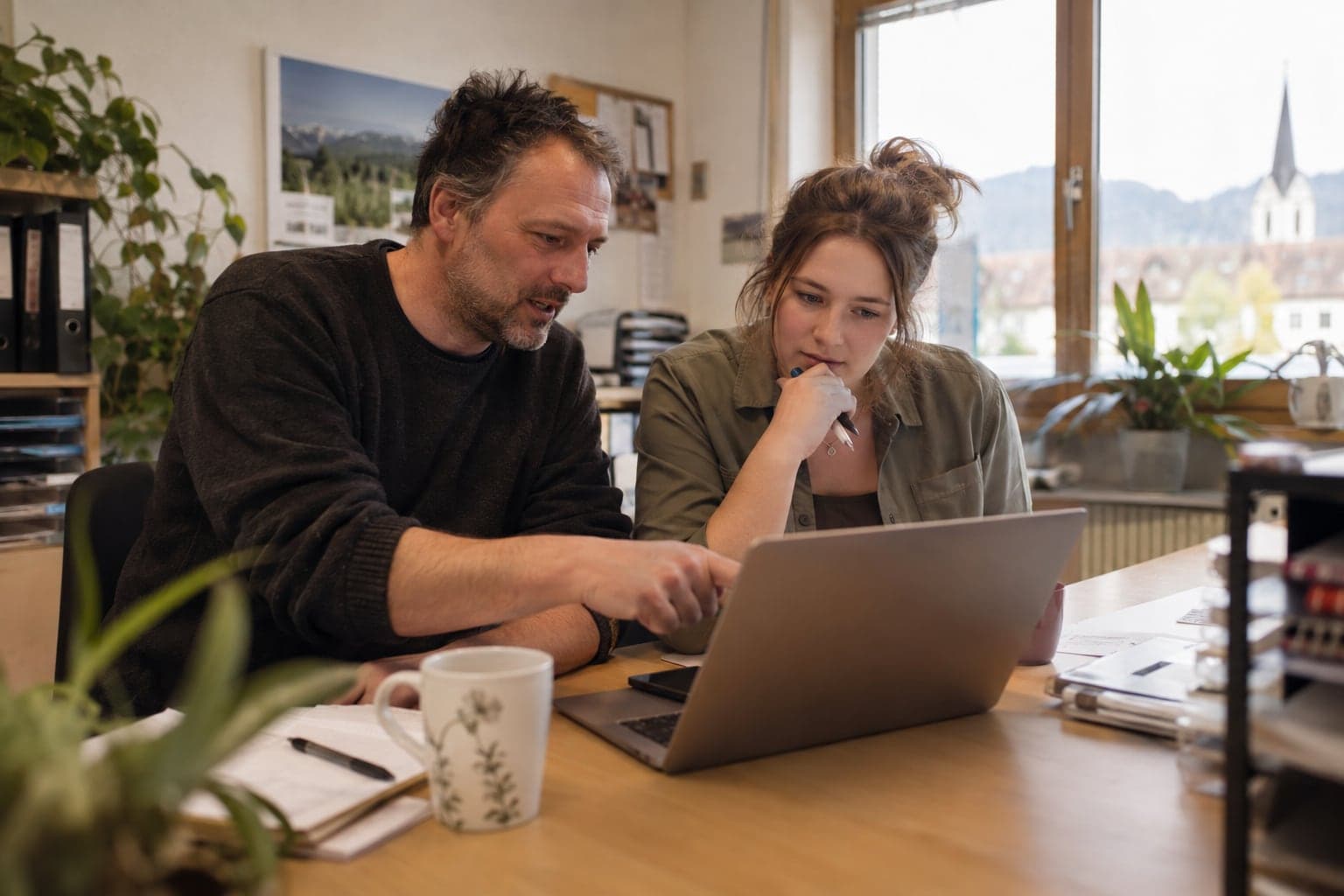 Ein Kollege zeigt einer neuen Mitarbeiterin im Innendienst am Laptop, wie Reklamationen bearbeitet werden.